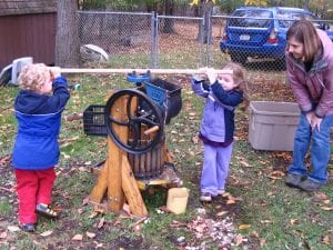 Two children press apple cider while a teacher looks on